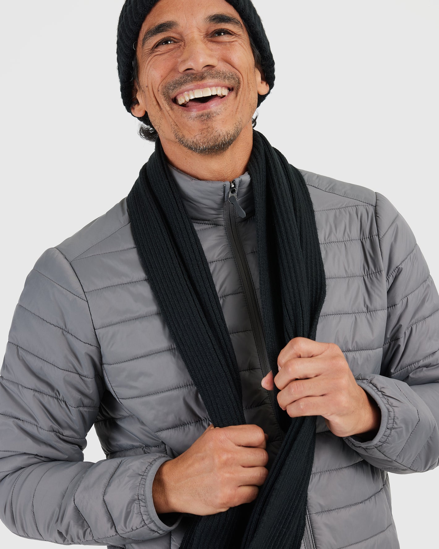 Person smiling, adjusting Black Sweater Scarf with winter layers.