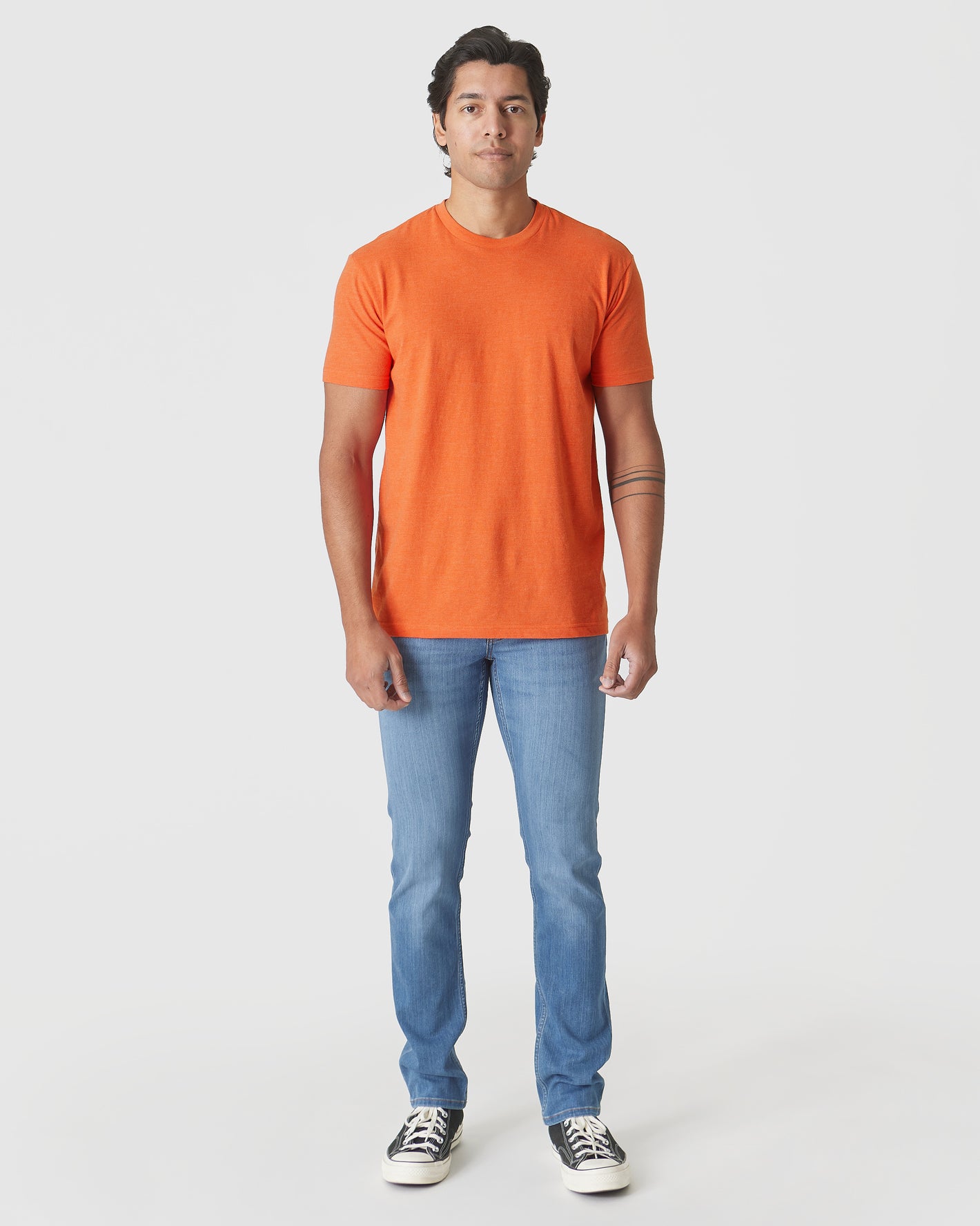 Man in Burnt Orange Heather Classic Crew Neck, slim jeans, canvas sneakers.