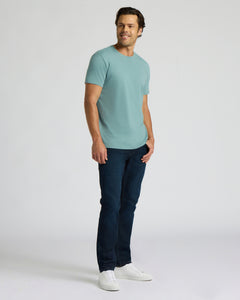 True ClassicA man modeling a light blue crew-neck t-shirt, dark blue jeans, and white sneakers against a plain light gray studio background.