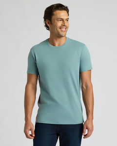 True ClassicA man wearing a light teal short-sleeve crewneck t-shirt and dark blue jeans, standing against a solid light gray background.