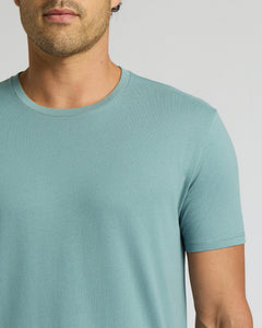 True ClassicA close-up of a man wearing a short-sleeve crew-neck t-shirt in a light teal blue color, shown from the chin down against a neutral light gray background.