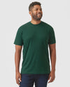 Man in Evergreen Heather Classic Crew Neck, smiling slightly, wearing dark jeans.