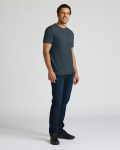 True ClassicA man modeling a dark slate blue crew-neck t-shirt, dark blue jeans, and black sneakers against a light gray studio background.
