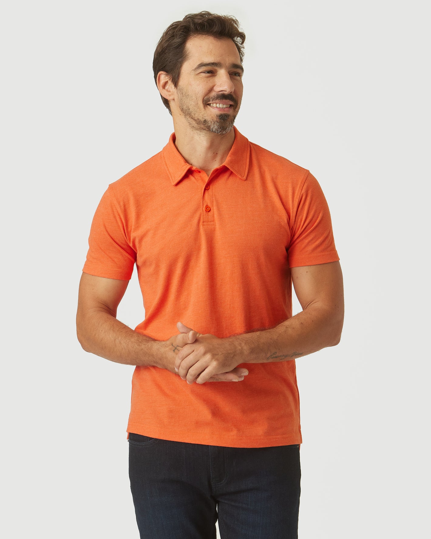 Man wearing Burnt Orange Heather Classic Polo, smiling with hands clasped.