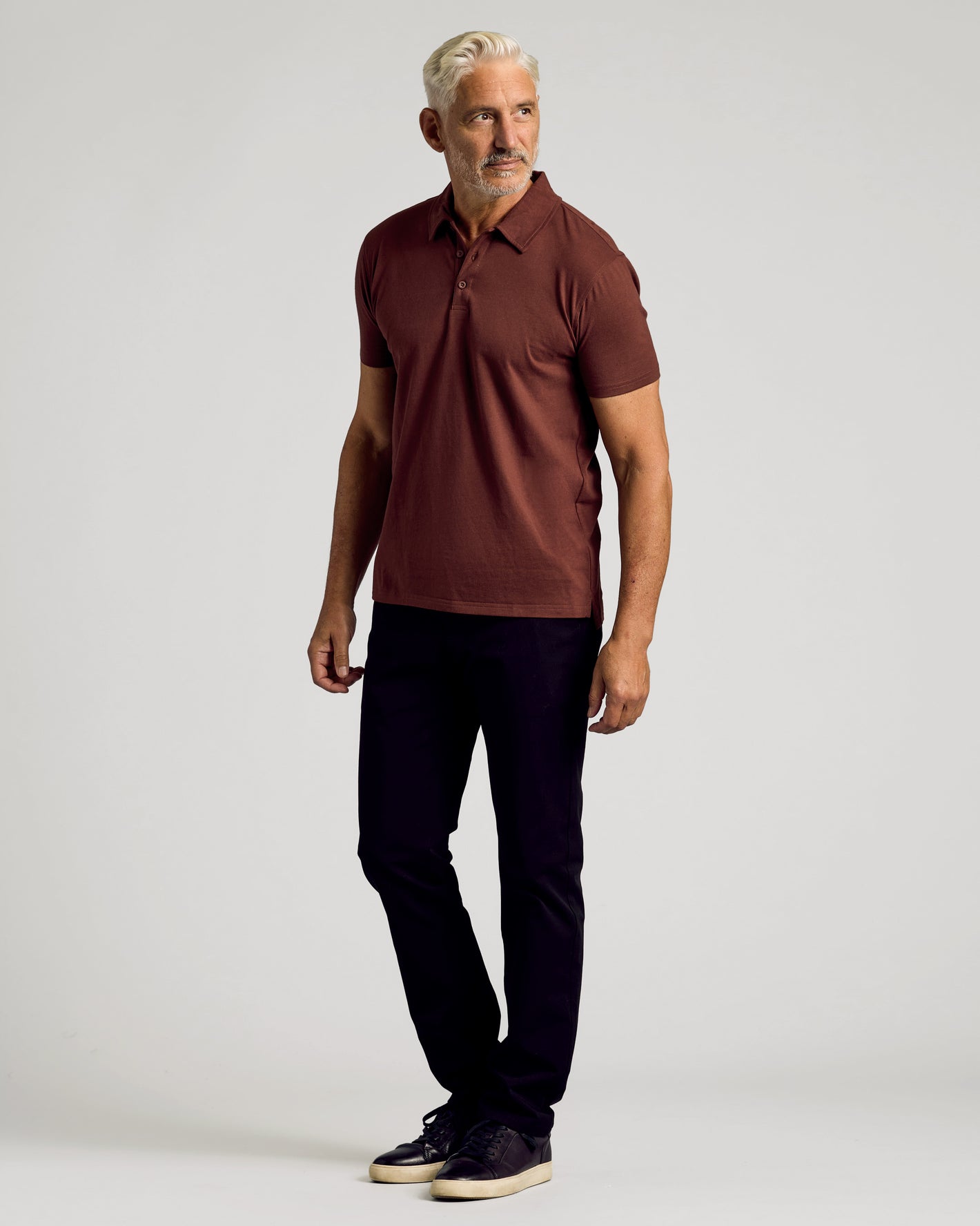 Man wearing Dark Chocolate Short Sleeve Polo with black trousers and sneakers.