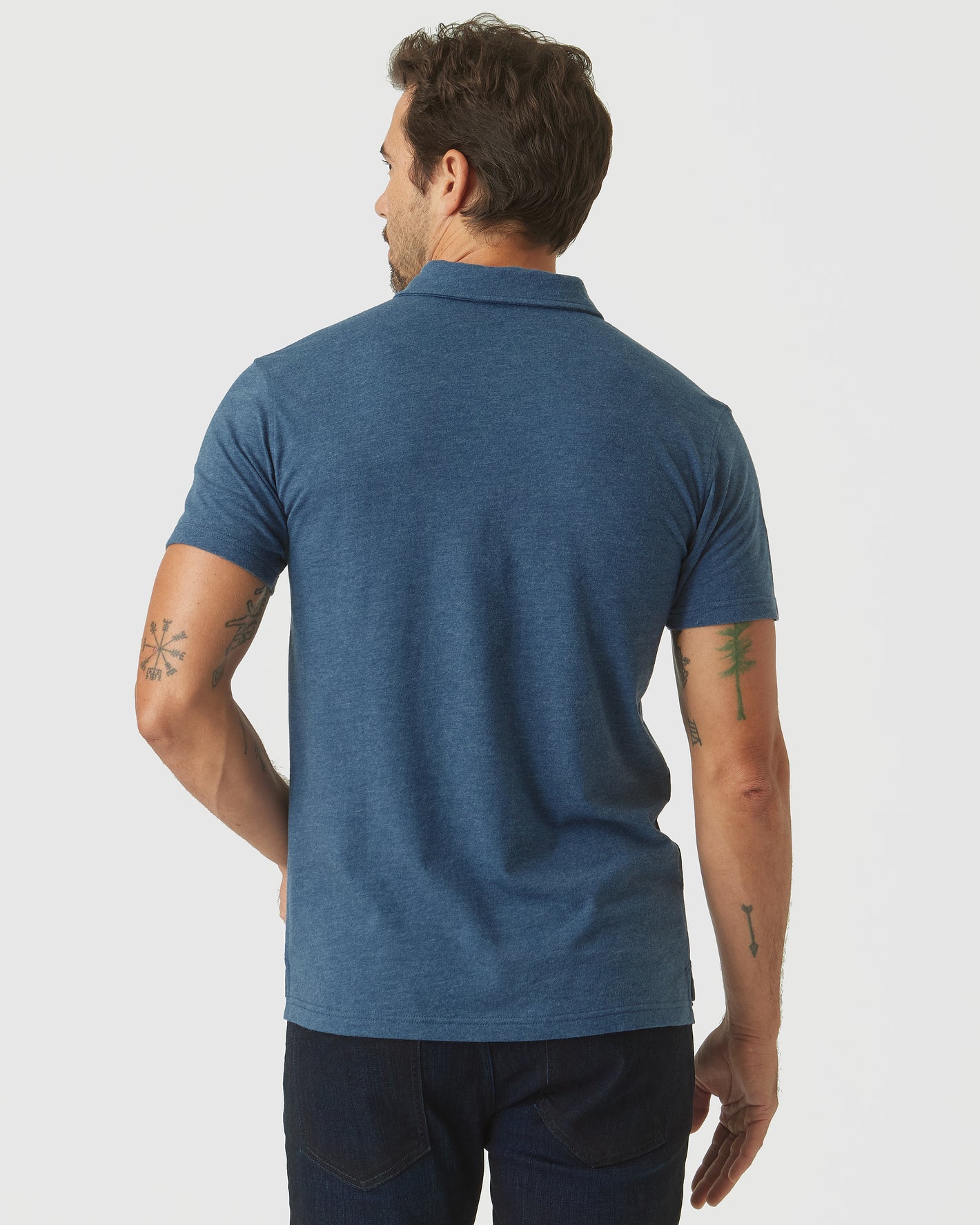 Man wearing Deep Sea Blue Heather Classic Polo, back view, tattooed arms visible.