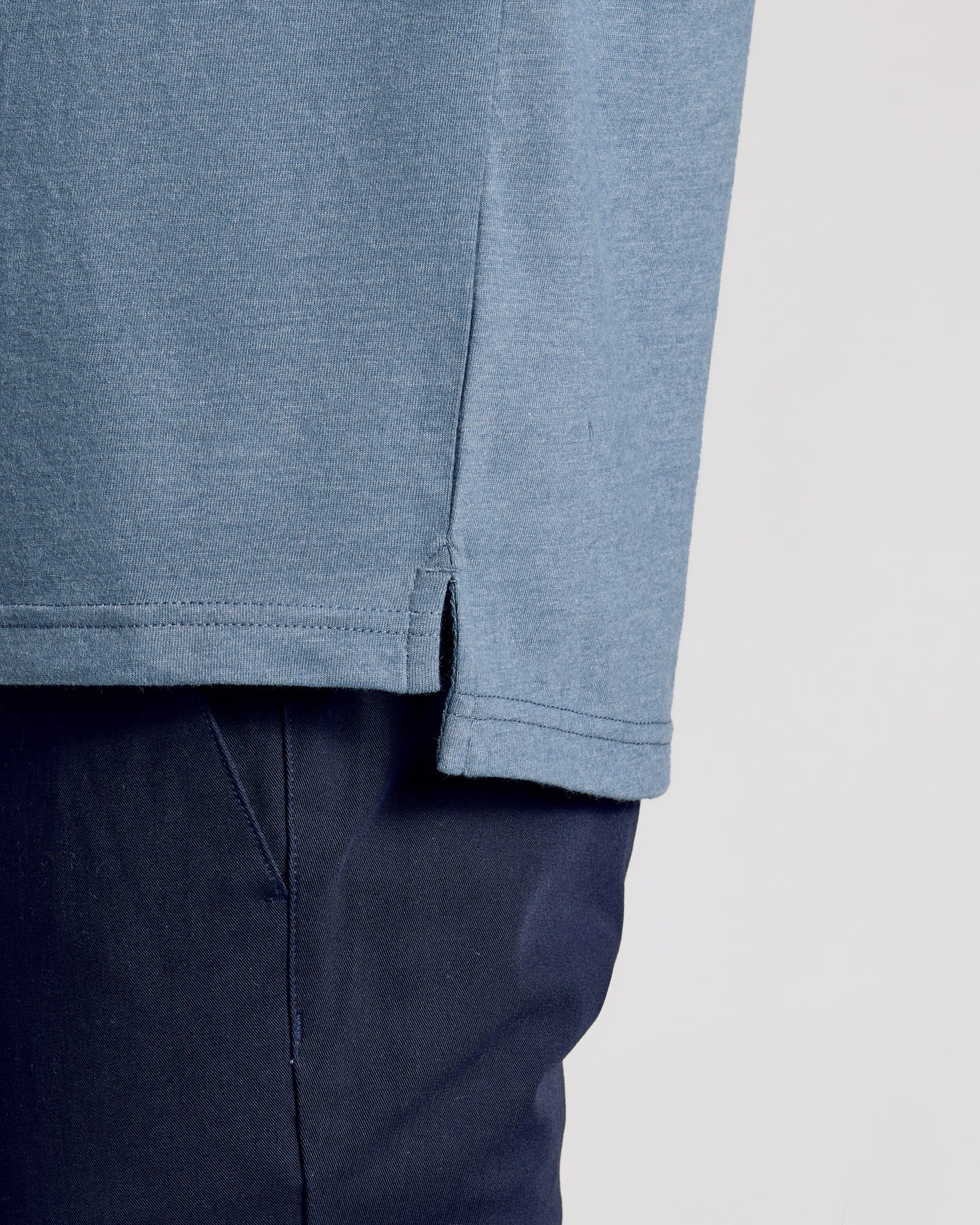Dark Heather Tempest Polo's hem with side slit over navy trousers.