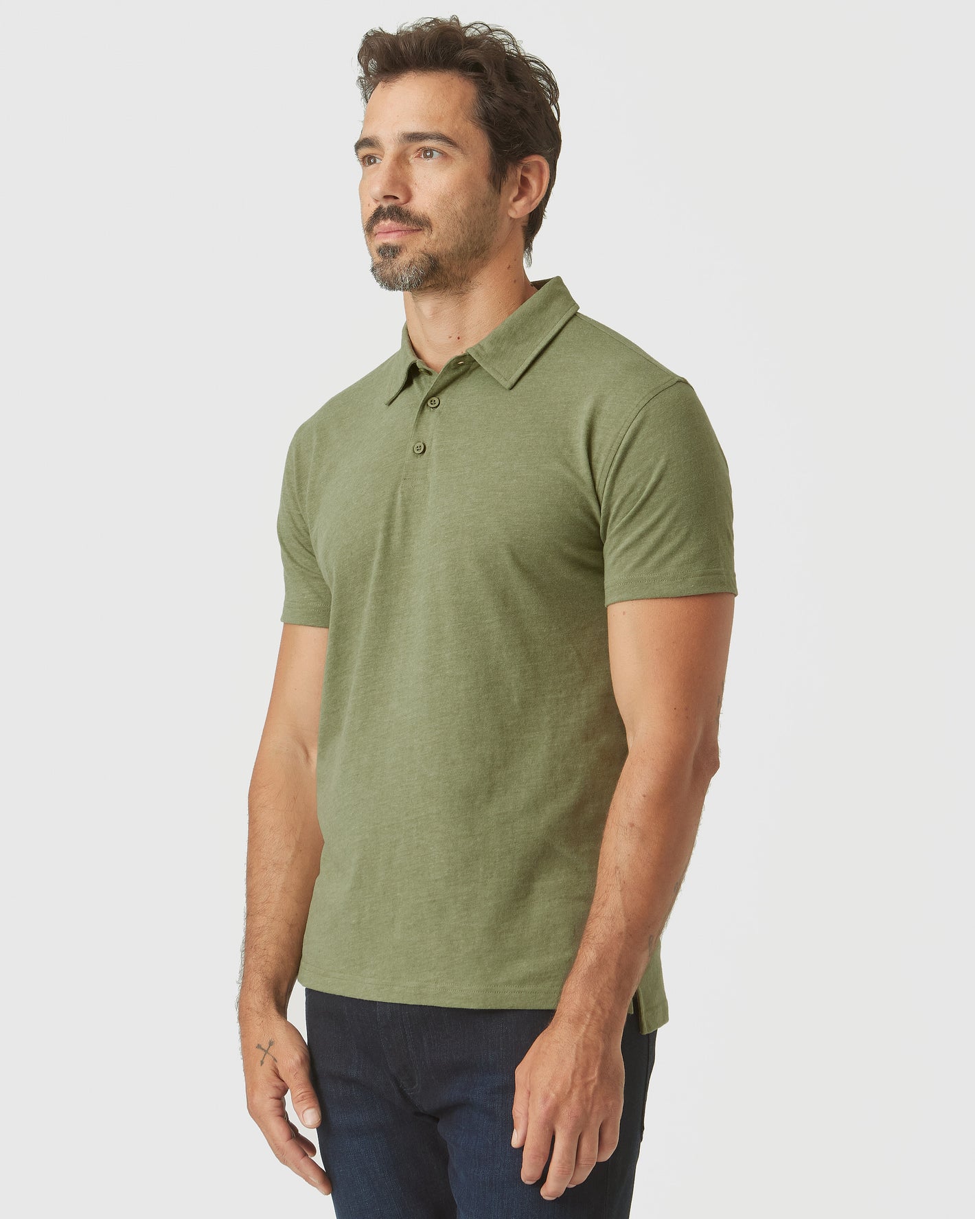 Model wearing Olive Green Heather Polo with dark trousers, gazing left.