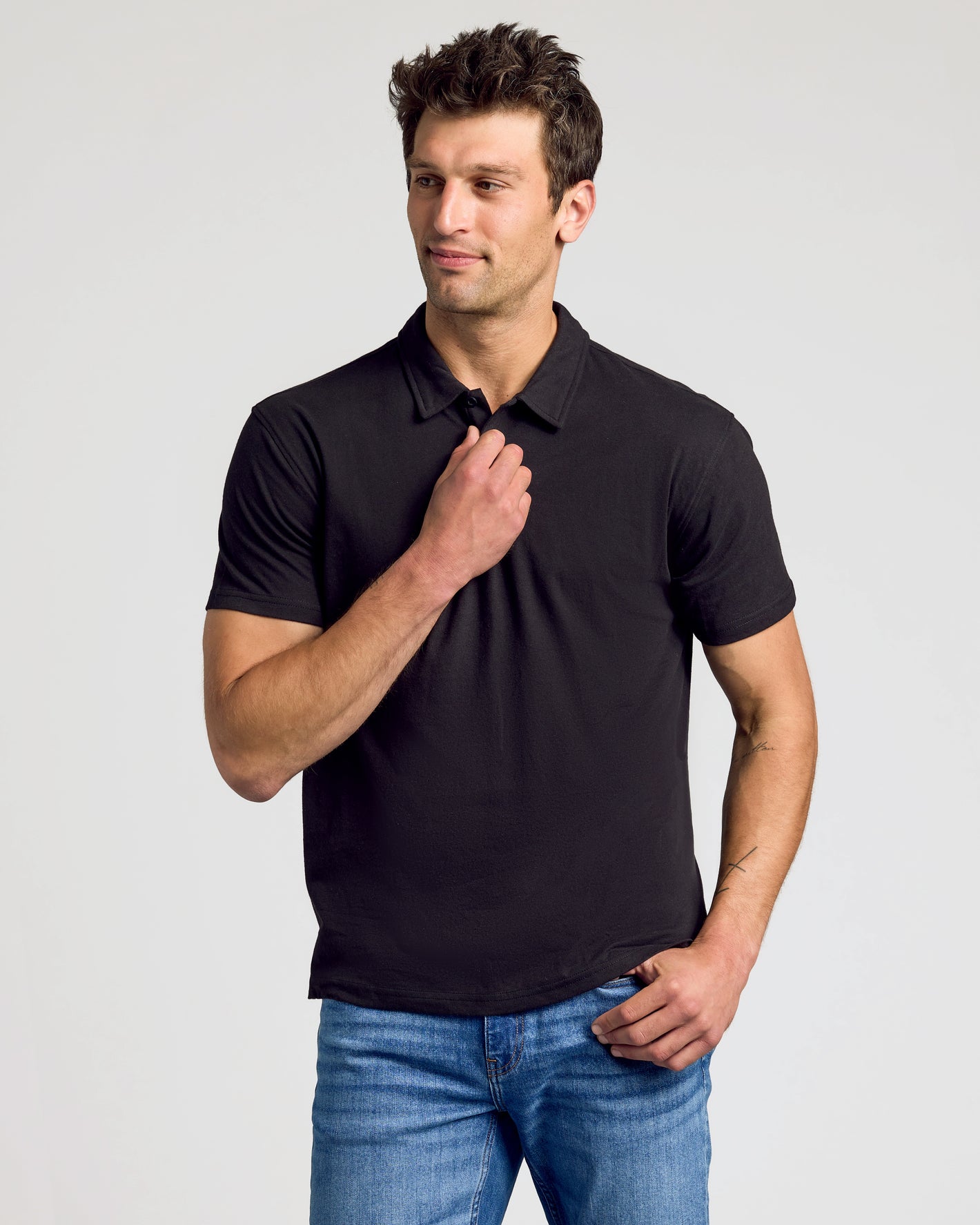 Man wearing Wardrobe Classic Polo 10-Pack: black short-sleeve polo, blue jeans.