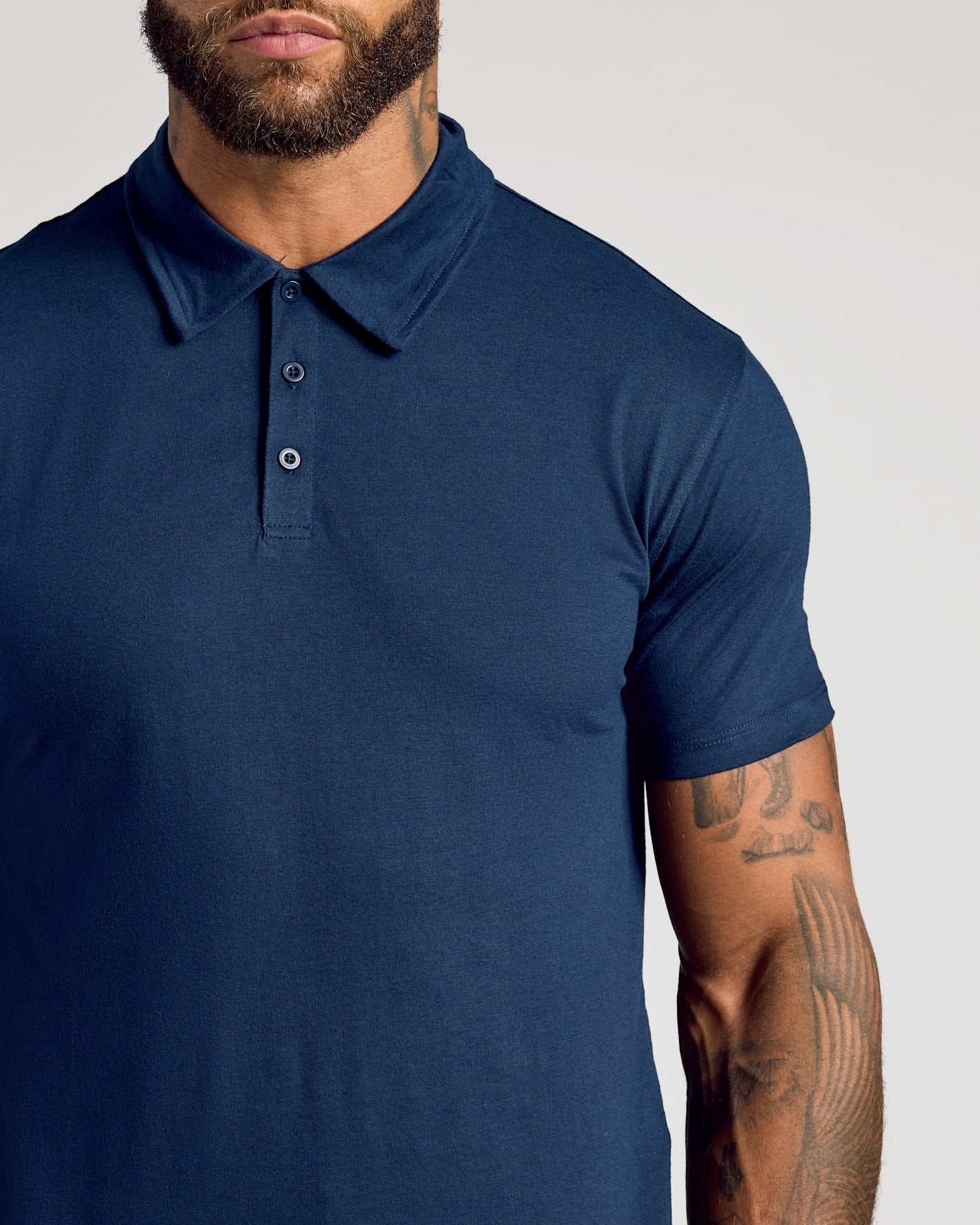 A close-up of a man wearing a navy blue short-sleeve polo shirt against a light gray background.