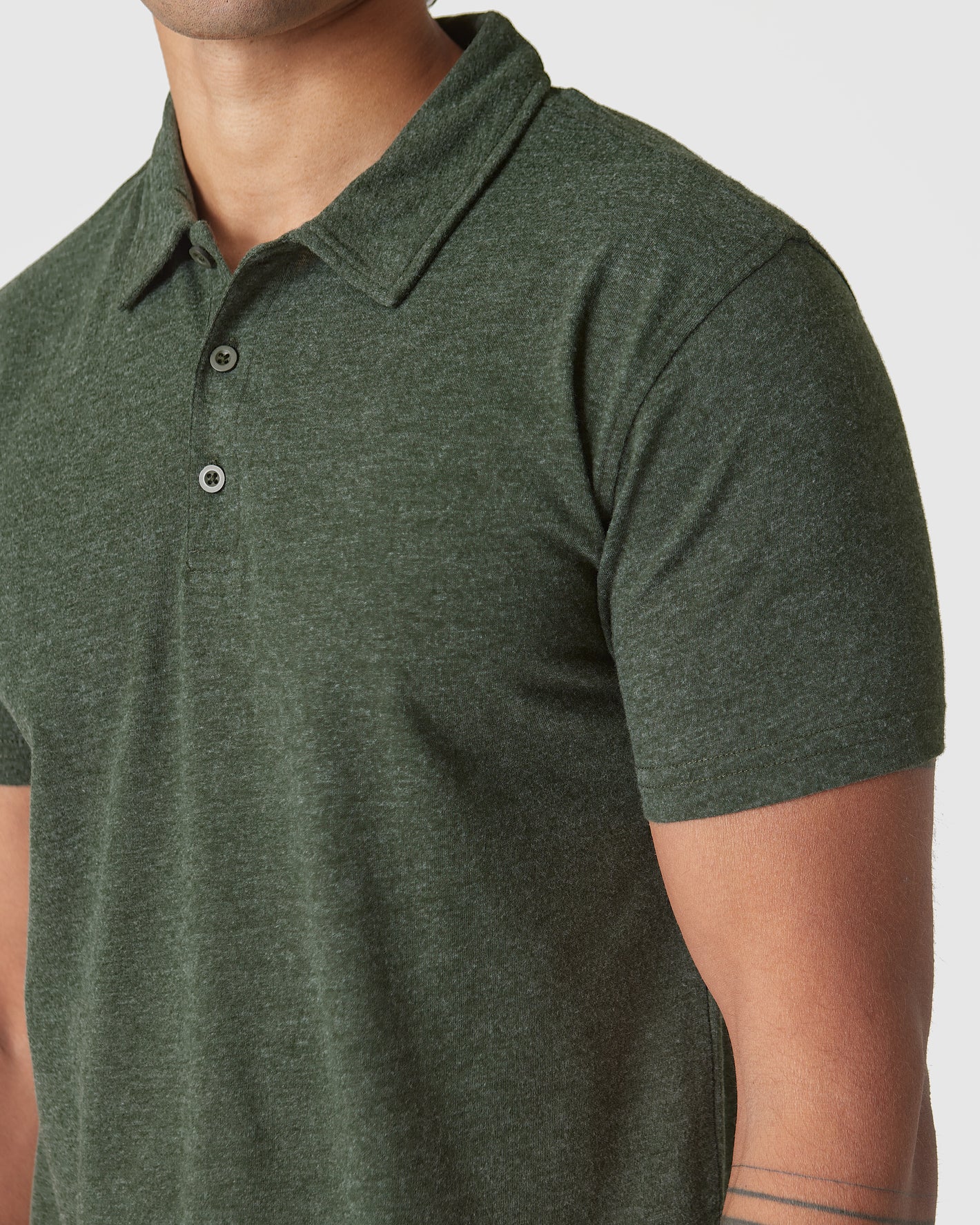 Person wearing Racing Green Heather Polo with collar and tattooed forearm visible.