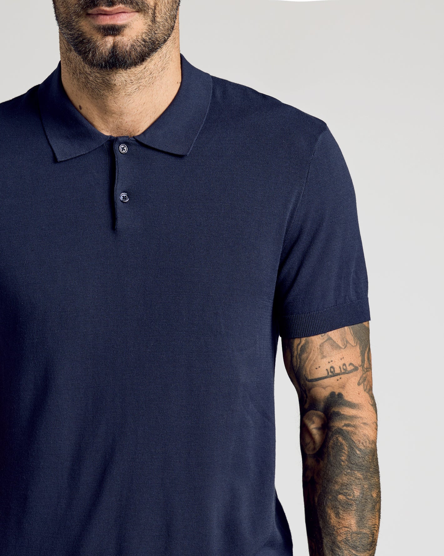 Bearded man wearing Navy Short Sleeve Sweater Polo with tattoos on forearm.