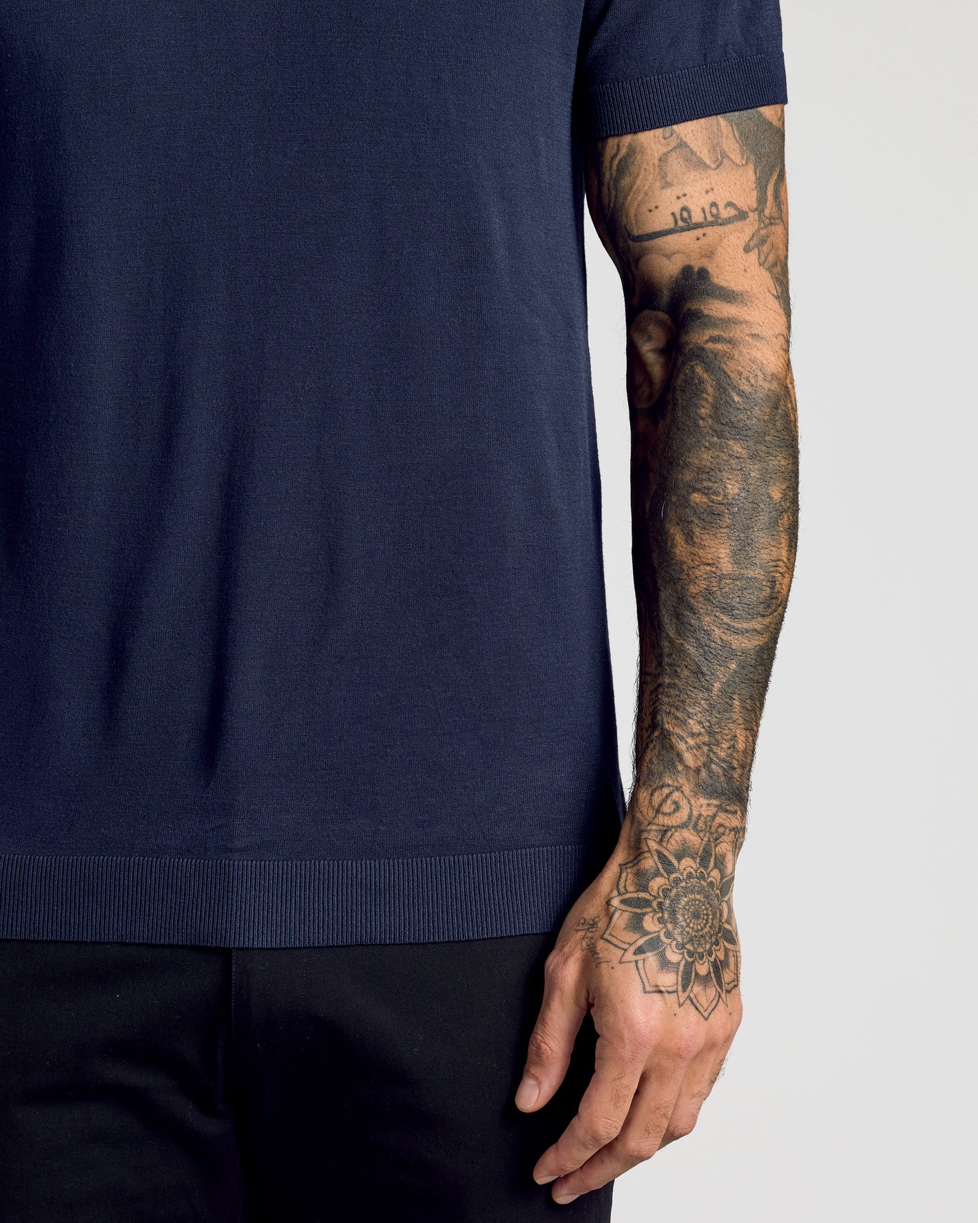 Navy Short Sleeve Sweater Polo over black trousers, showcasing detailed tattoos.