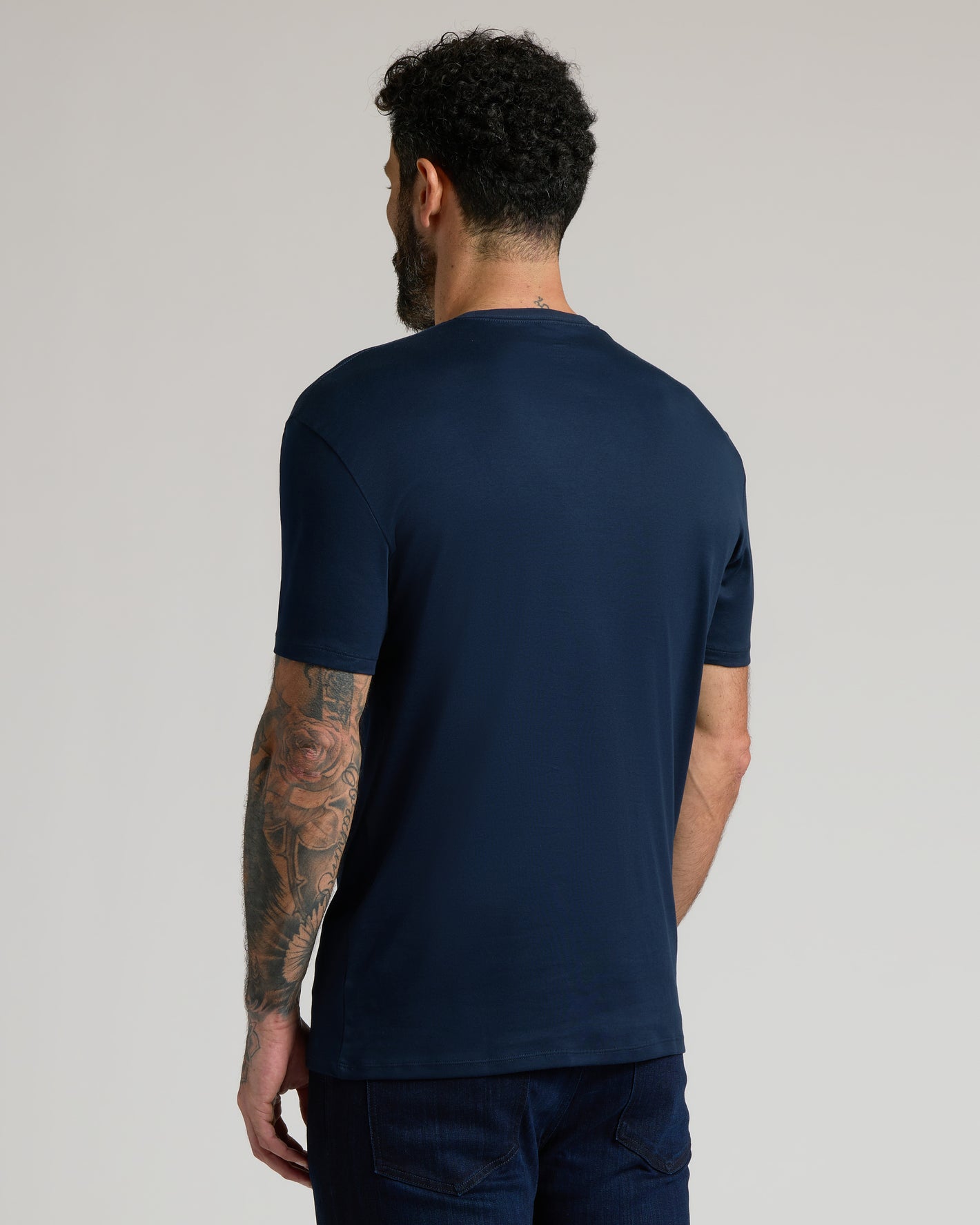Man in Navy & Ether Premium Pima Crew Neck T-Shirt, tattooed arm visible.