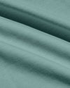 A close-up of draped fabric in a muted sage green color, showing the texture and weave with soft folds.