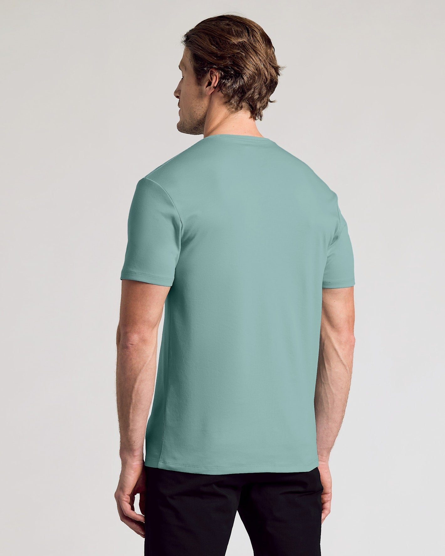 A man wearing a short-sleeve crewneck t-shirt in a muted sage green color, shown from the back against a light gray studio background.