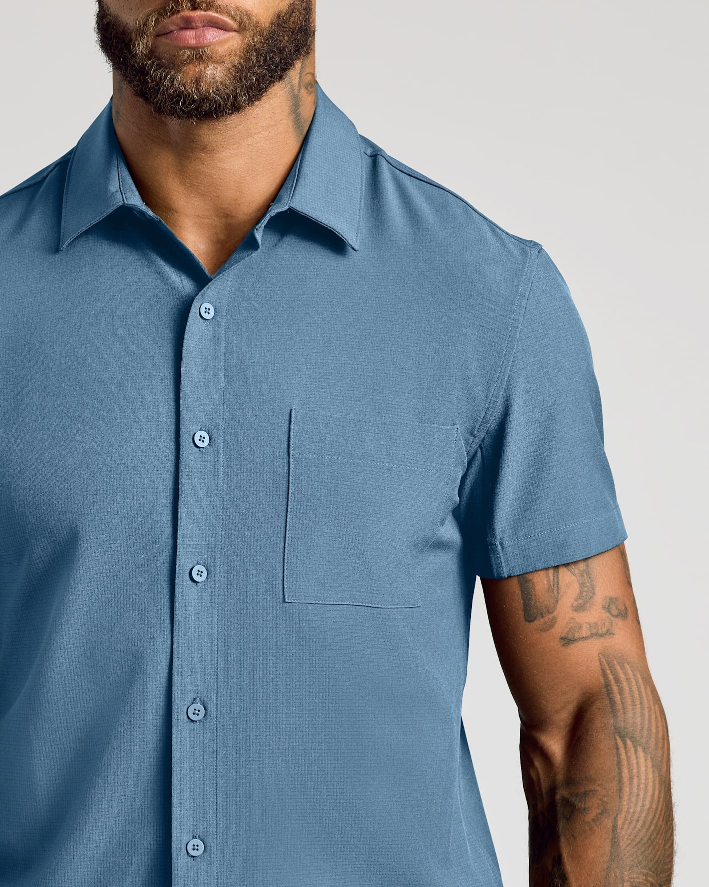 Man wearing Navy & Fiord Short Sleeve Ripstop Commuter Shirt, showcasing tattoos.