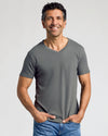 A smiling man wearing a gray v-neck t-shirt and blue jeans.