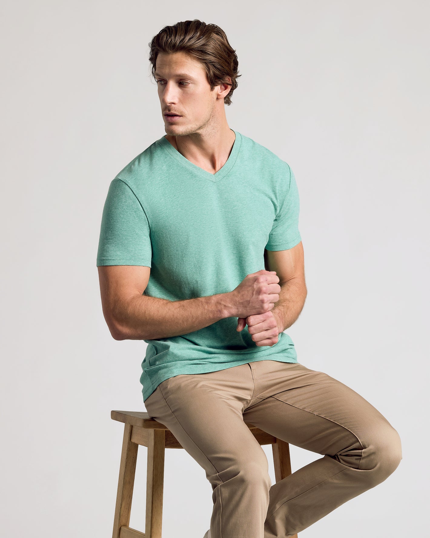Young man wearing Light Heather Greenery Classic V-Neck, seated casually.
