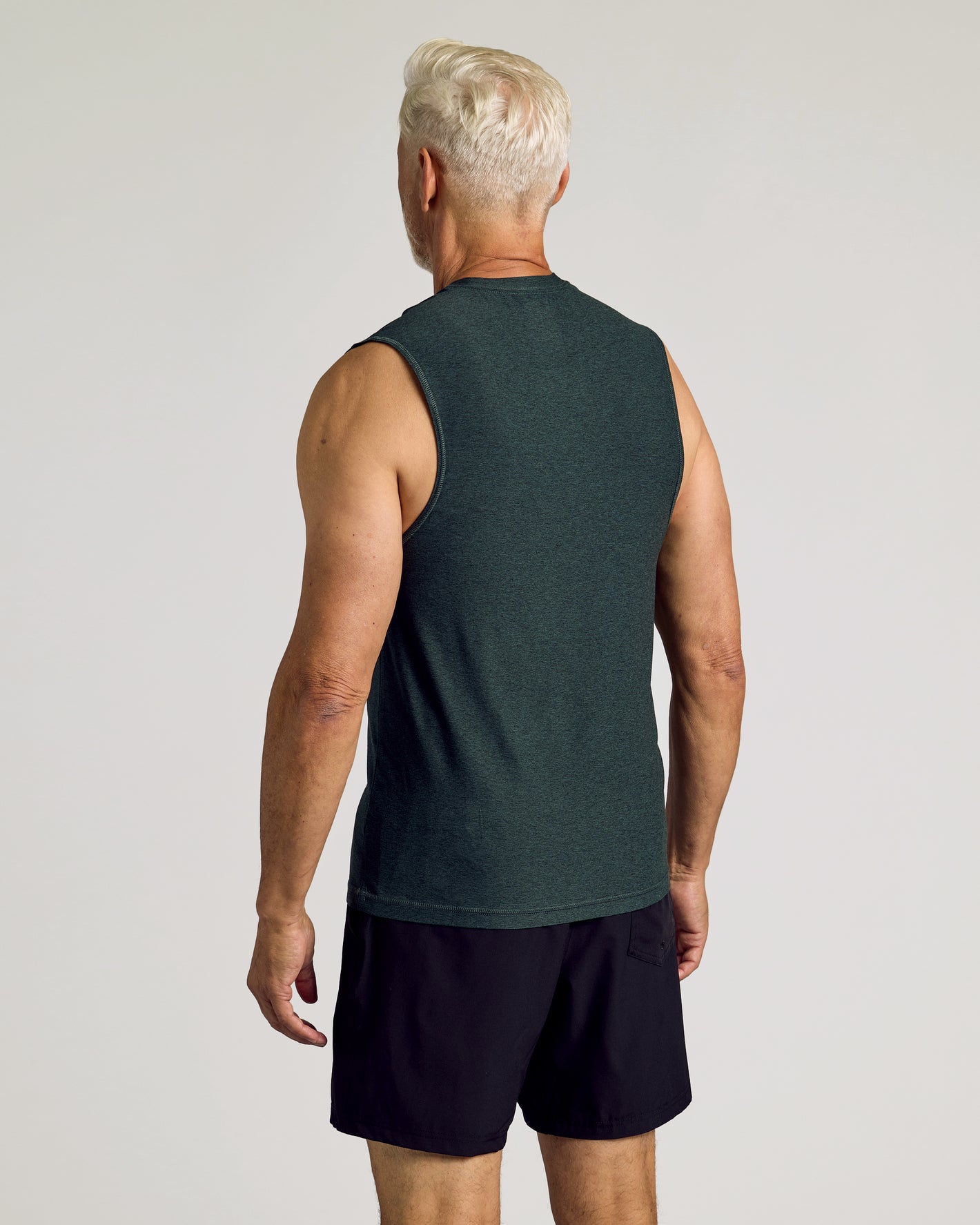 Man wearing Dark Heather Forest Sleeveless Active Muscle Tee, back view.