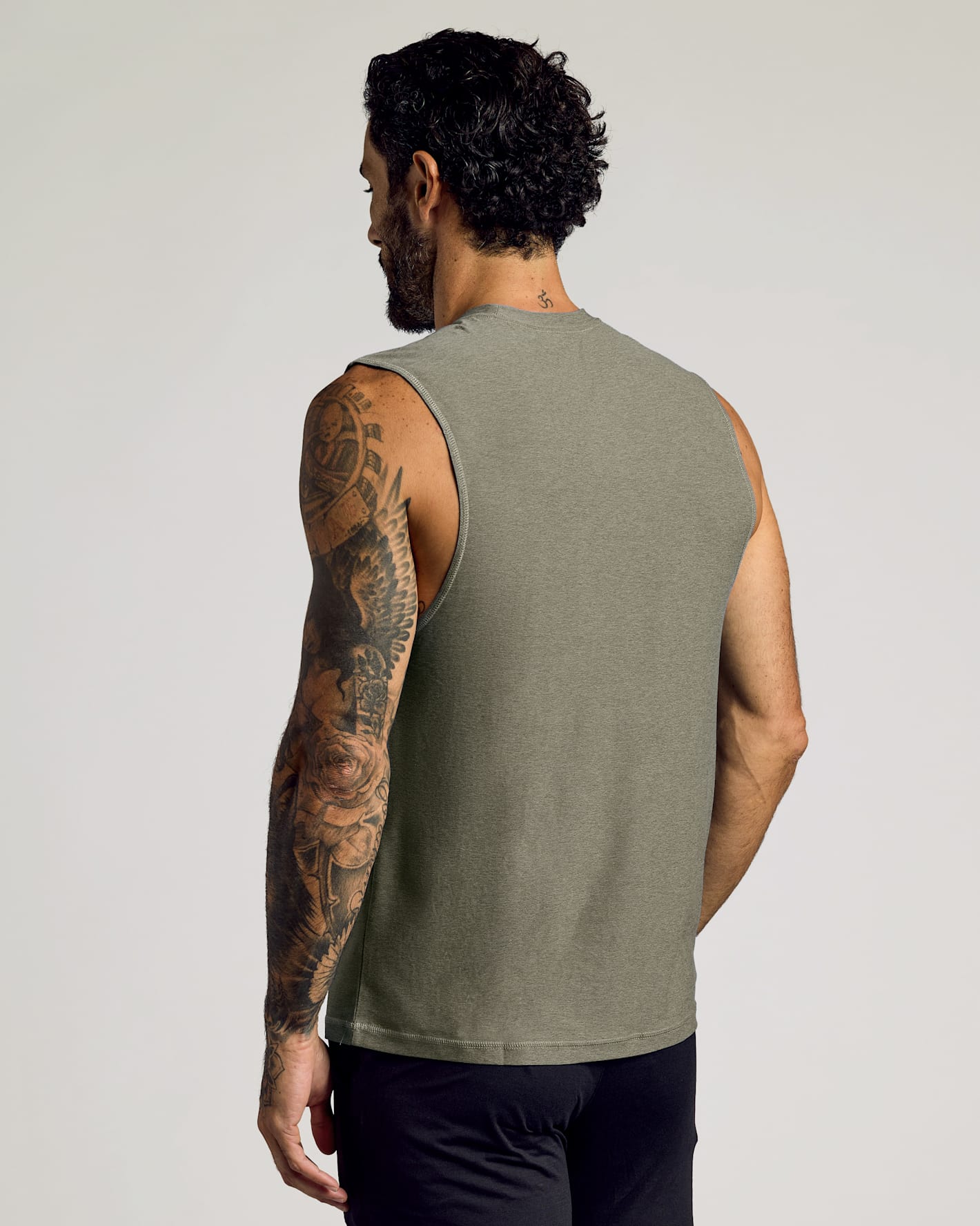 A man with tattoos on his left arm wearing a Heather Military Green Sleeveless Active Muscle Tee, shown from the back, highlighting the fitted sleeveless design and soft fabric.