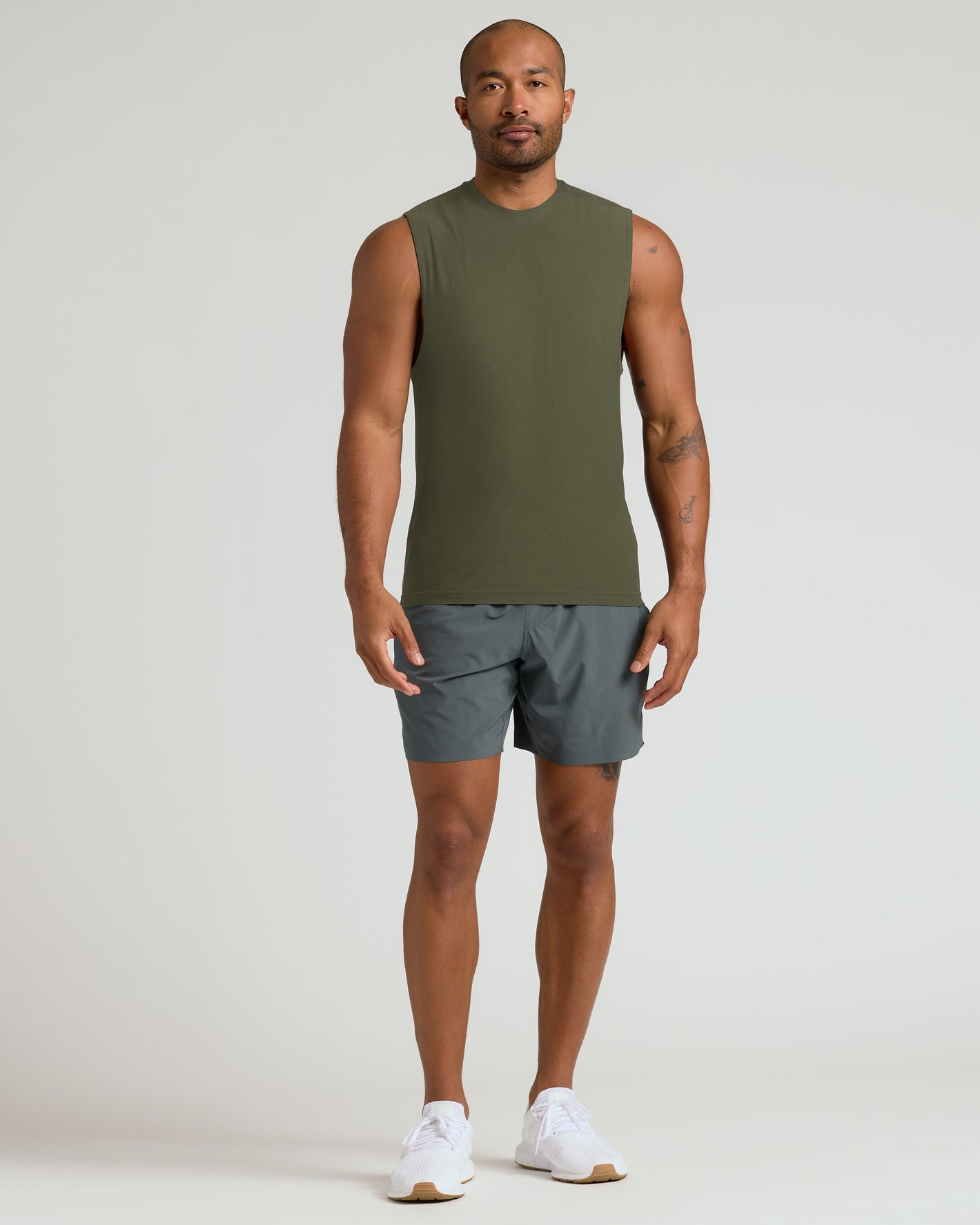 Model wearing Military Green Sleeveless Active Muscle Tee, paired with charcoal shorts.