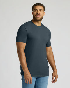 True ClassicA man wearing a dark slate blue crewneck t-shirt and light blue jeans, standing against a light gray studio background.