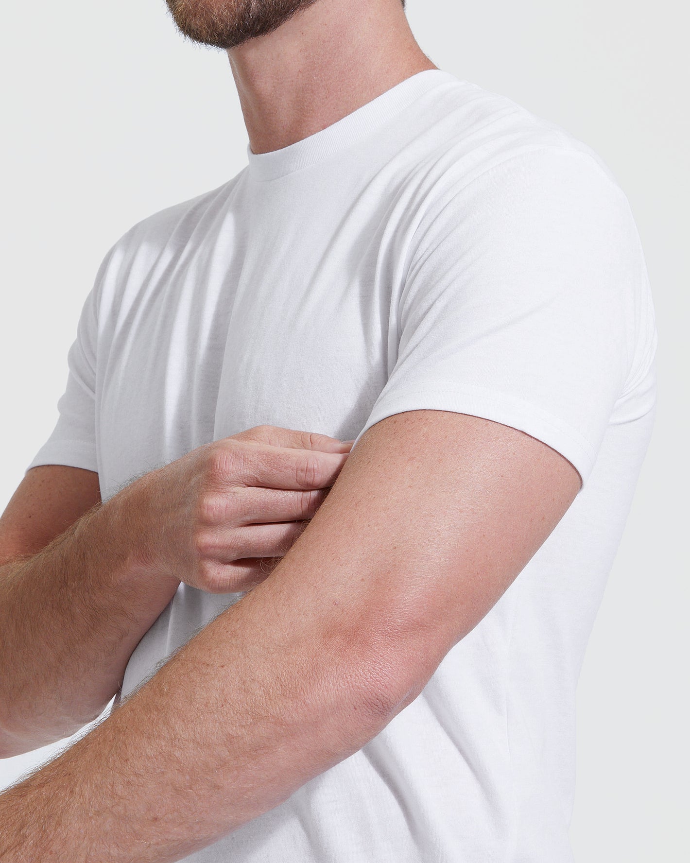 Man wearing All-White Tall Straight Hem Crew Neck T-Shirt, adjusting sleeve.