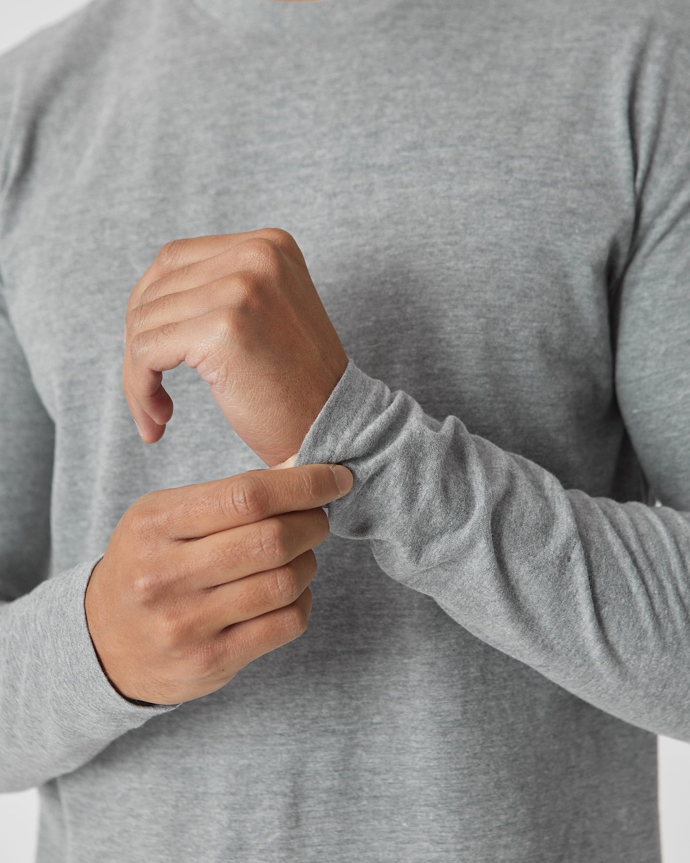 Close-up of a person wearing a light gray long-sleeve crewneck shirt, adjusting the cuff of one sleeve with both hands.