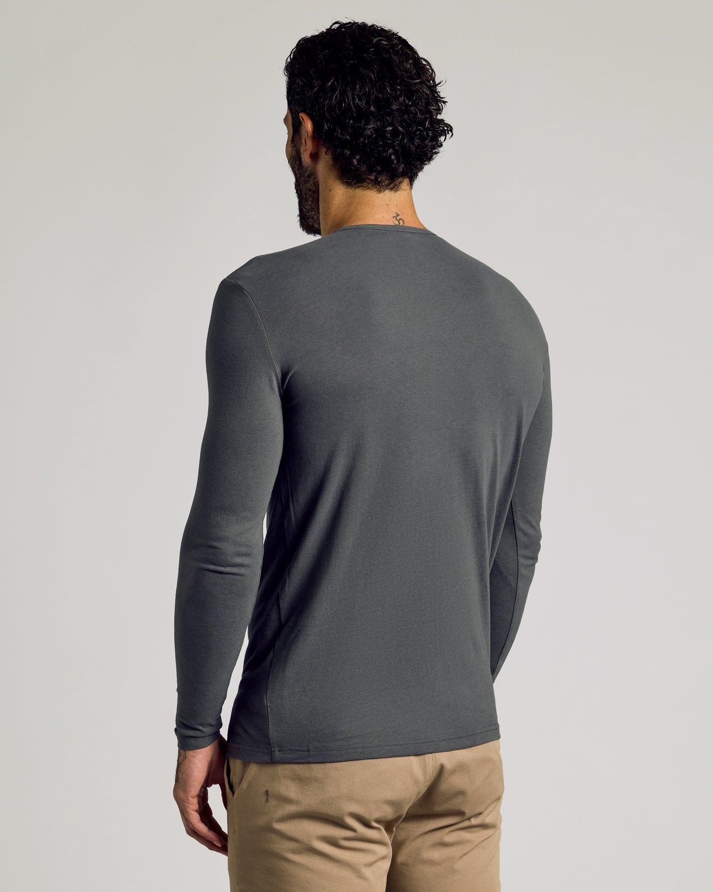 Man wearing Carbon Tall Classic Long Sleeve Henley and tan pants, back view.