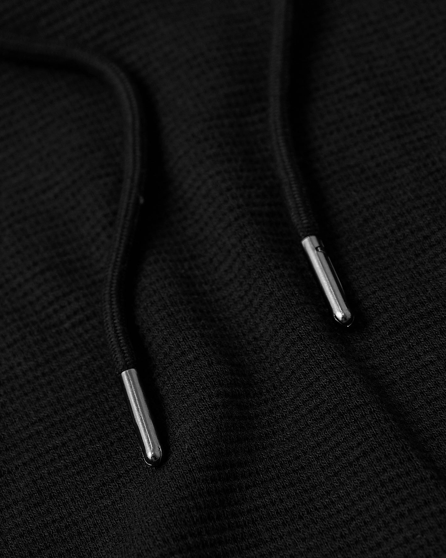 Black Tall Waffle Hoodie drawcords with silver metal aglets on textured fabric.
