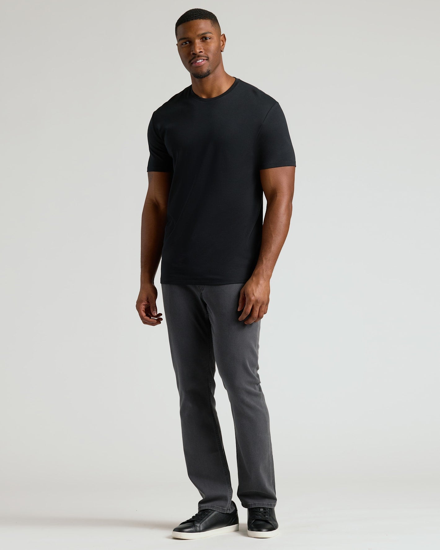 Man wearing a black crew neck t-shirt styled with gray pants and black sneakers, showcasing the Tall Pima Cotton Blend Crew 4-Pack as a comfortable men's basic essential.