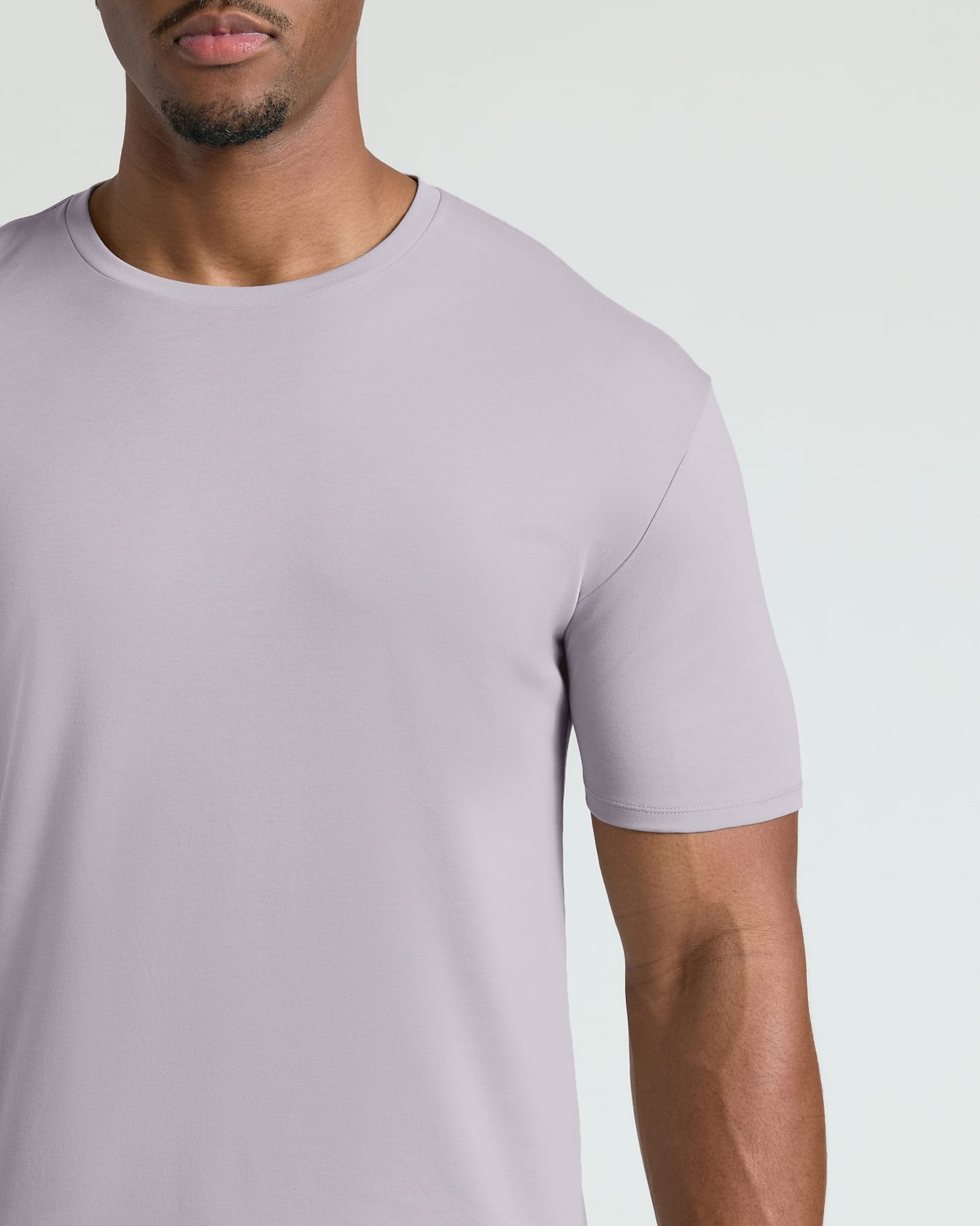 A close-up of a man wearing a light lavender crew-neck t-shirt against a plain light gray background.