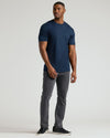A man wearing a navy blue Tall Pima Cotton Blend Crew 4-Pack t-shirt paired with gray pants and black sneakers, standing against a plain light background.