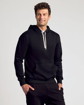 Man in Black Fleece French Terry Pullover Hoodie, hands in pockets, smiling.