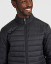 Man in Black Puffer Jacket, zipped to stand collar, smiling.