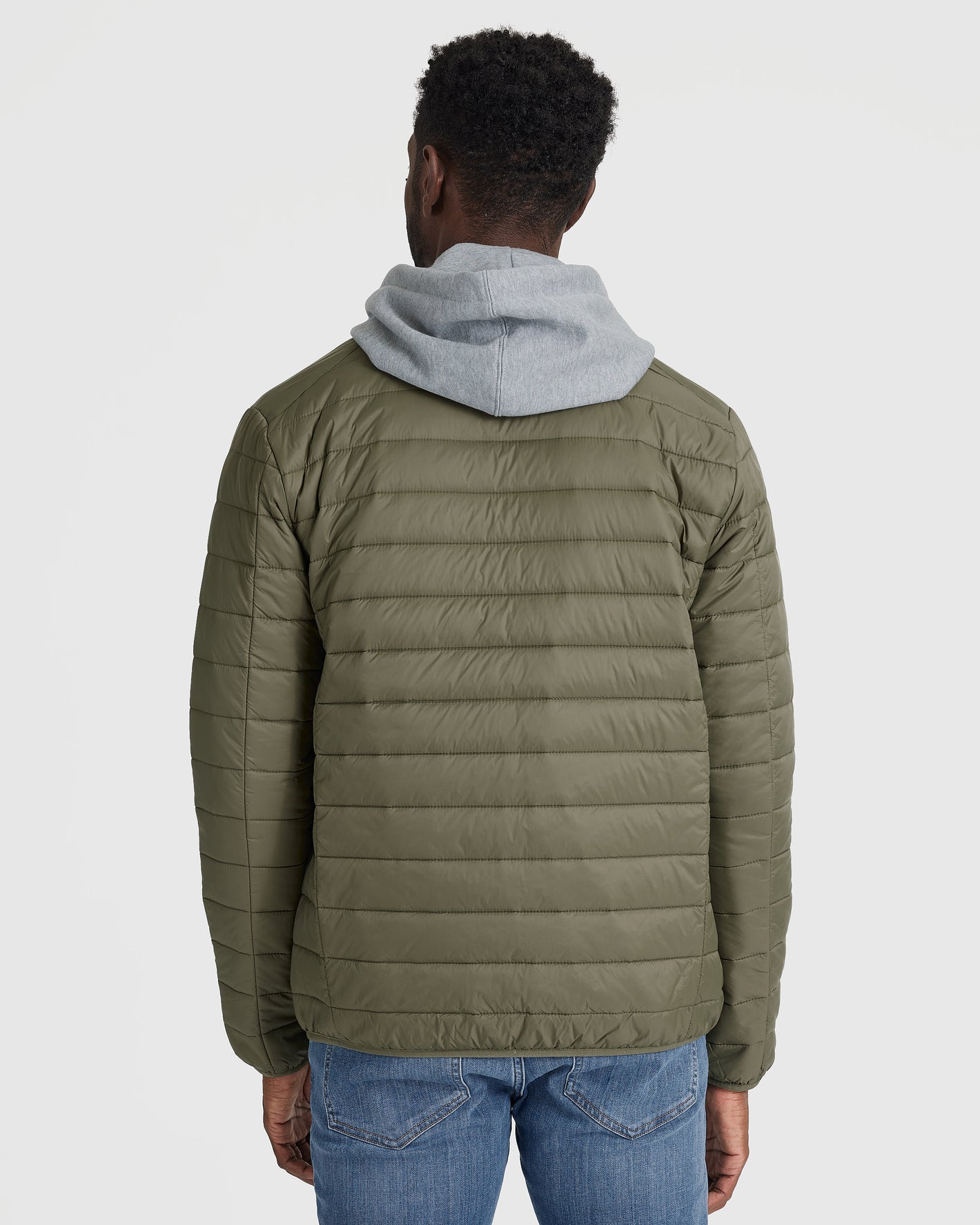 Man wearing Military Green Puffer Jacket, gray hoodie, blue jeans.