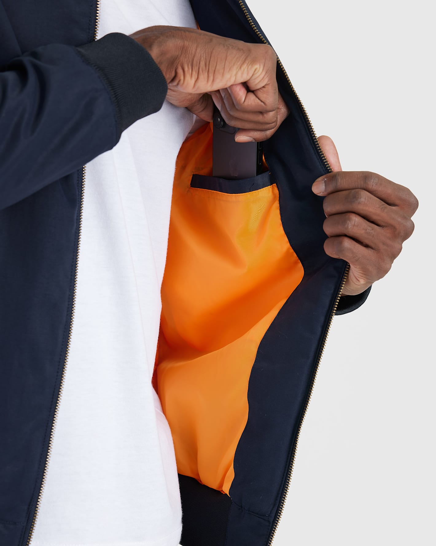 Unzipping Navy Bomber Jacket to slip phone into inner chest pocket.