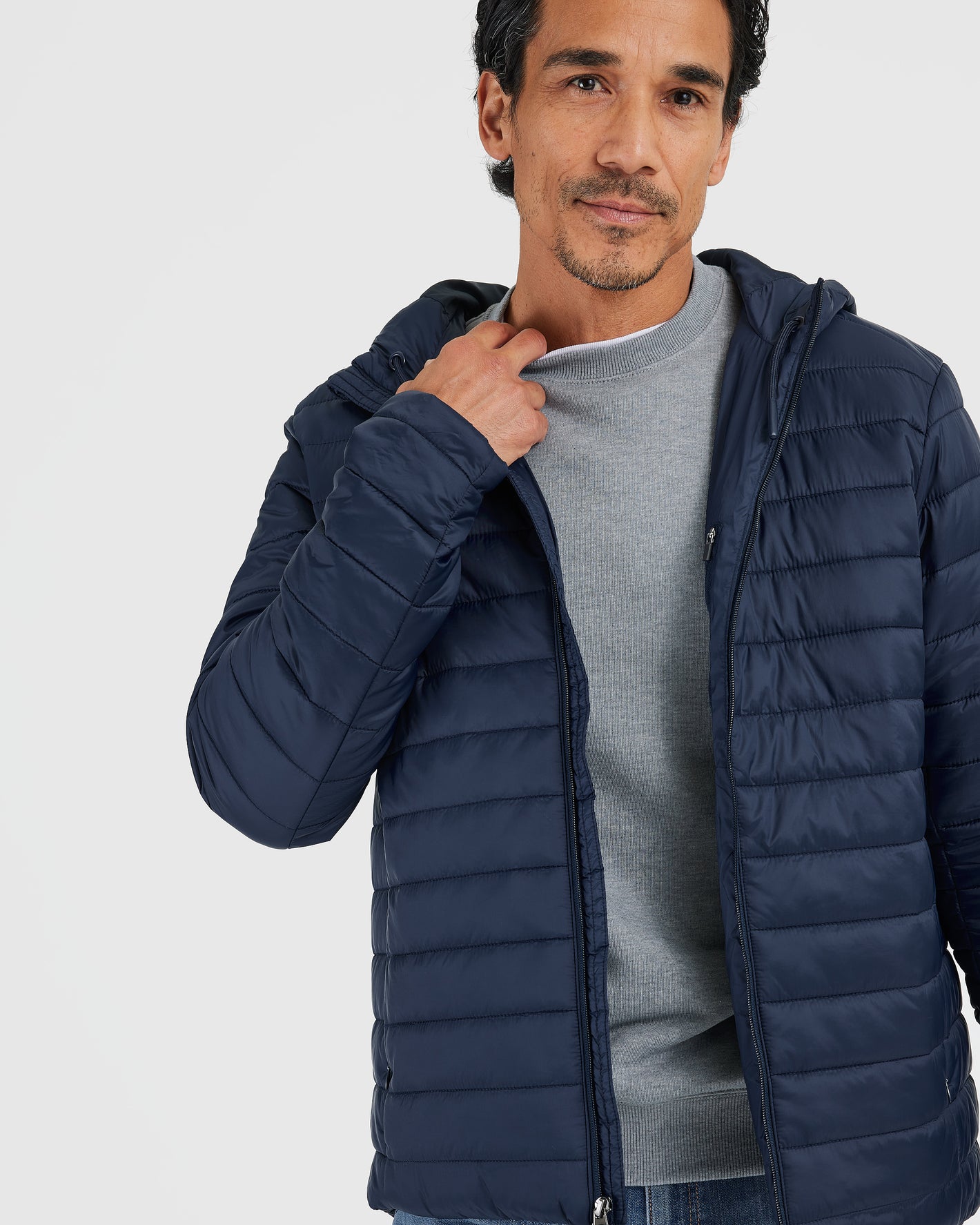 Man adjusting Navy Hooded Puffer Jacket over light gray sweater.