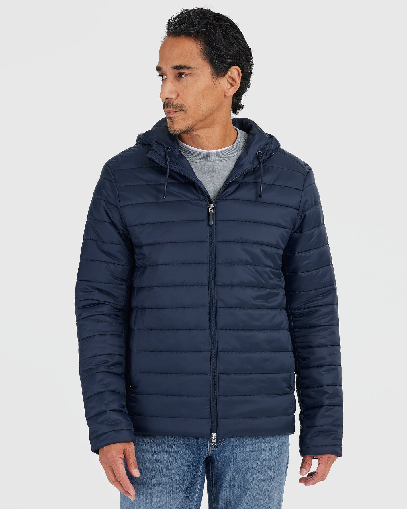 Man wearing Navy Hooded Puffer Jacket over gray sweatshirt, blue jeans.
