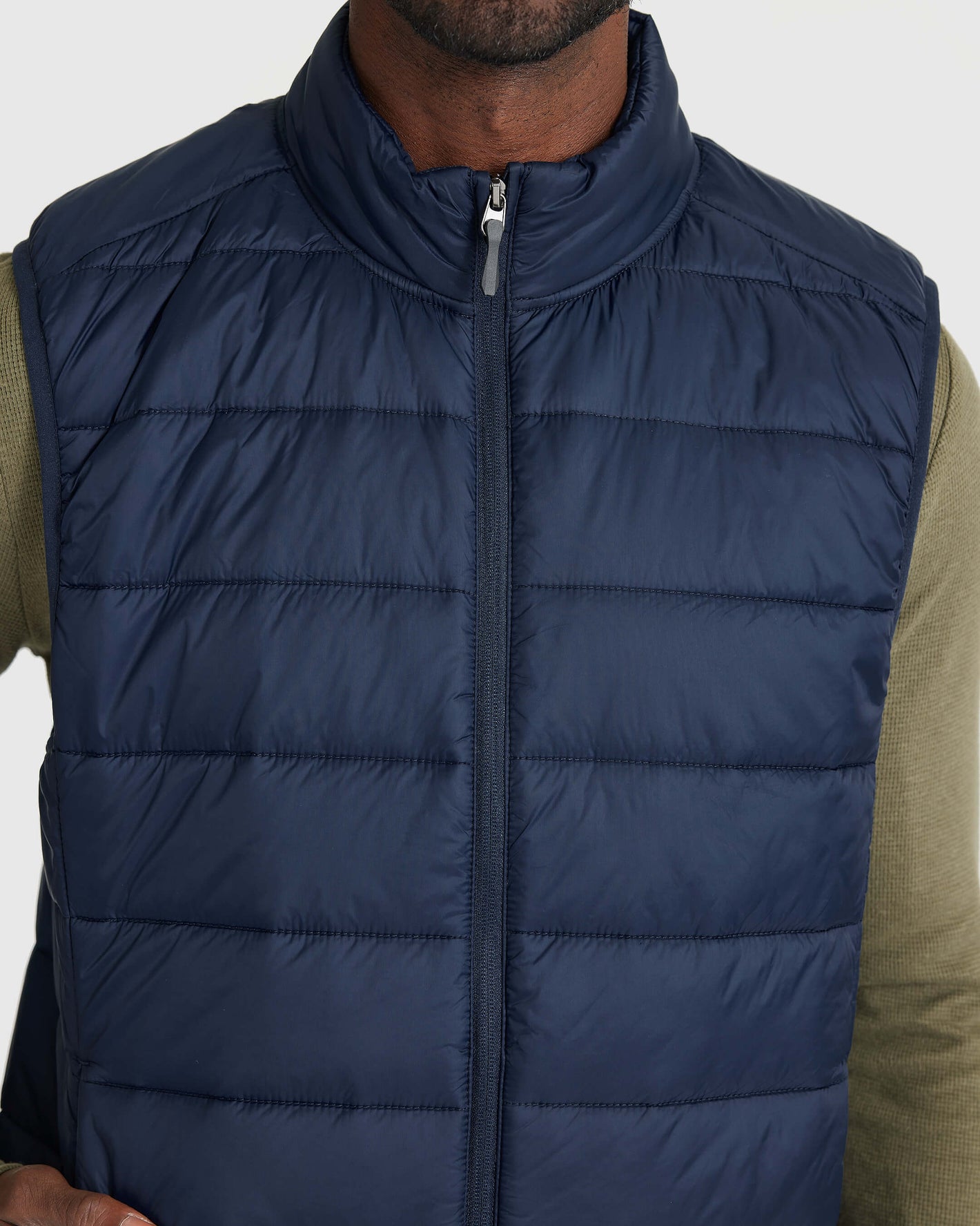 Navy Puffer Vest over olive shirt, showing zipper and quilted design.