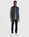 Man wearing Navy Puffer Vest over olive shirt with jeans.