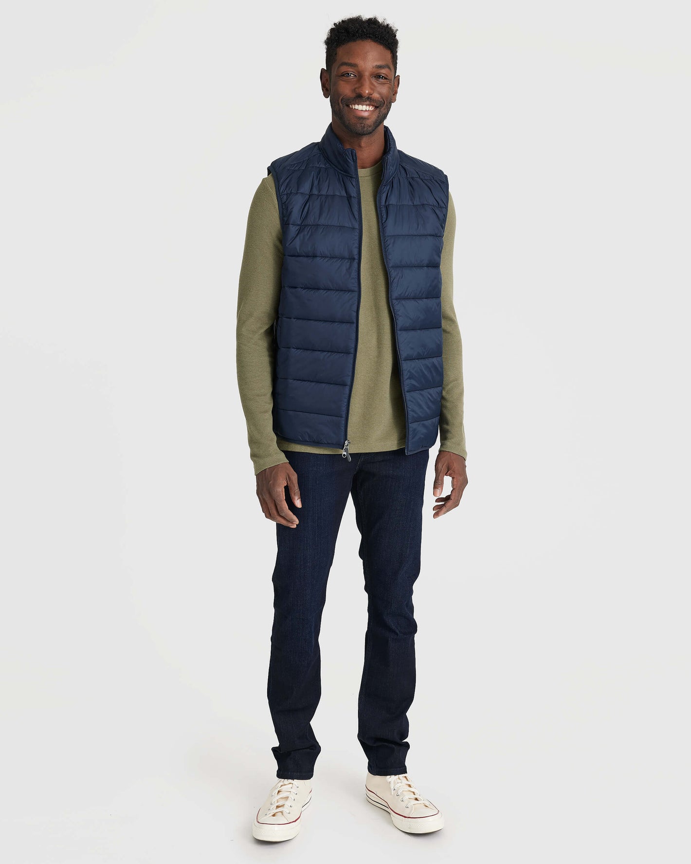 Man wearing Navy Puffer Vest over olive shirt with jeans.