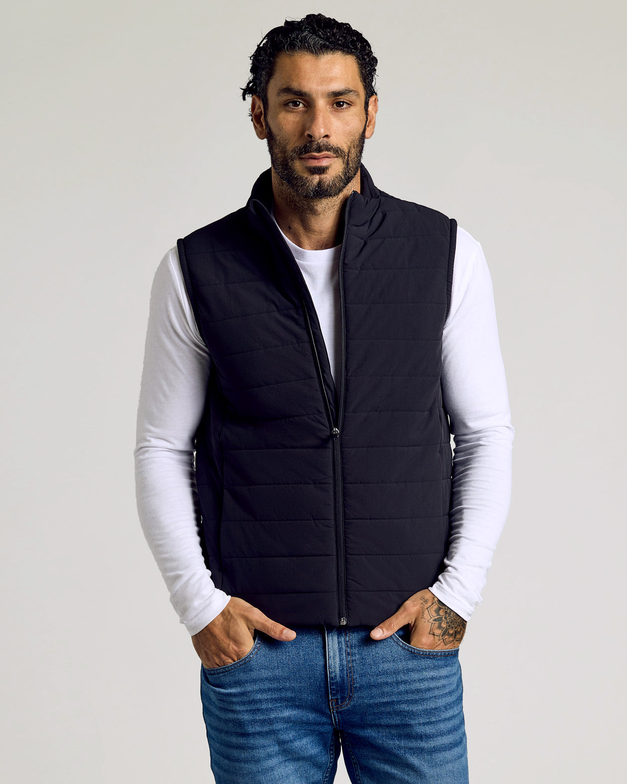 Man wearing Black Puffer Vest over white shirt, hands in pockets.