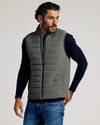 Man wearing a gray Carbon Puffer Vest over a black long-sleeve shirt and blue jeans, showcasing a casual and comfortable men's basics look.