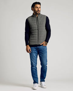 True ClassicMan wearing a grey Carbon Puffer Vest over a black long-sleeve shirt paired with blue jeans and white sneakers, standing against a plain background.
