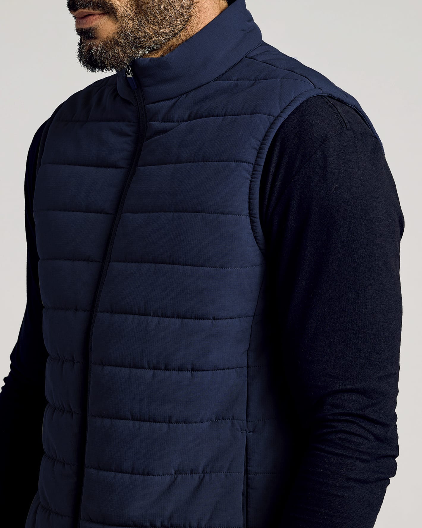 Close-up of a man wearing a Navy Puffer Vest over a long-sleeve black shirt, showcasing its quilted design and high collar for a sleek, modern look in men's basics.