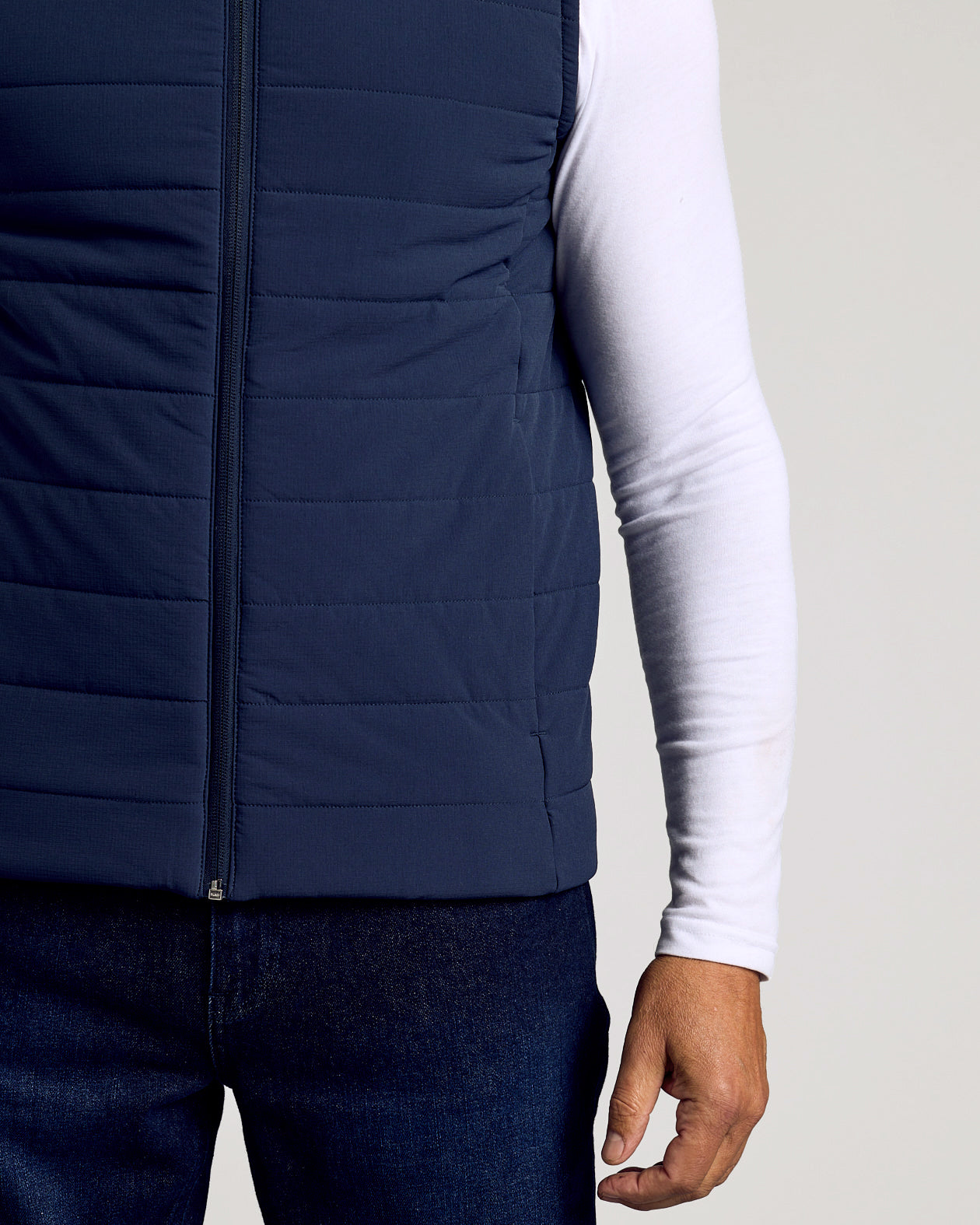 Navy Puffer Vest over white shirt, dark jeans, hand at side.