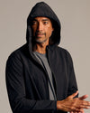 Man wearing Black Tech Windbreaker with hood up, looking sideways.