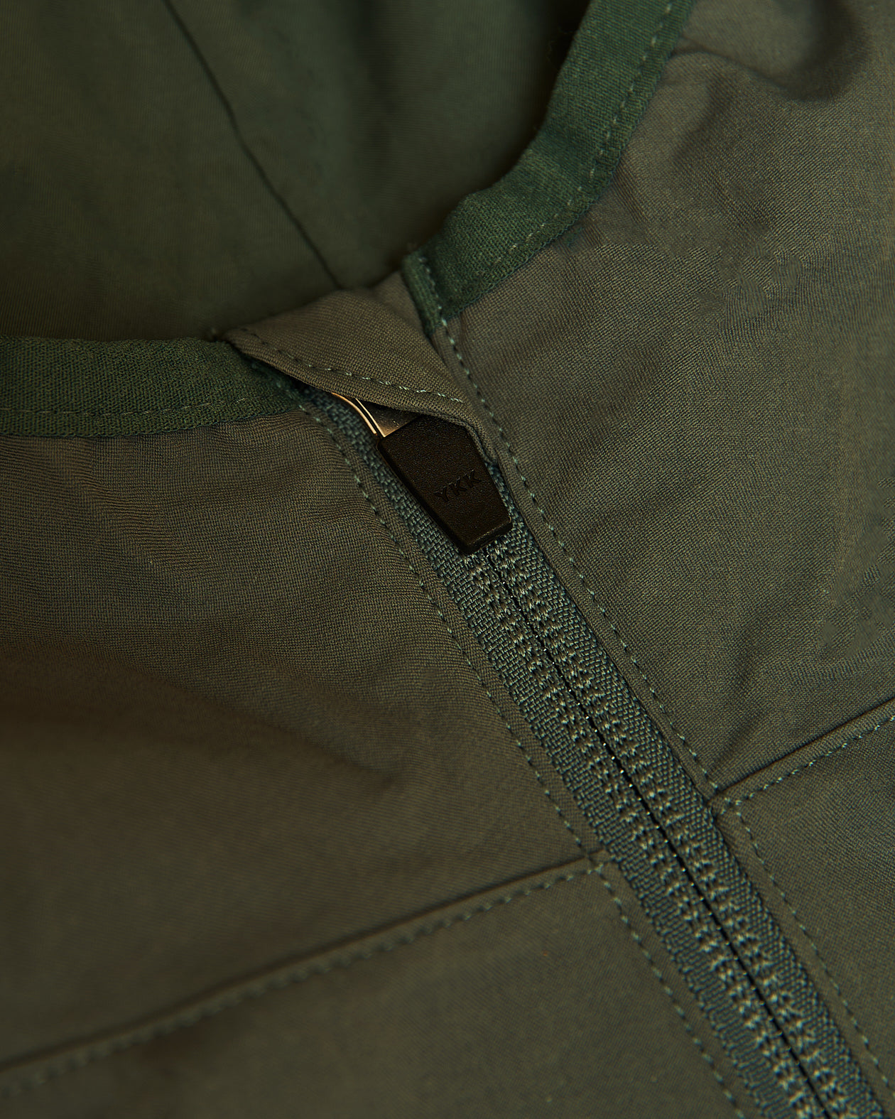 Olive Tech Windbreaker close-up, highlighting front zipper and stitched panels.